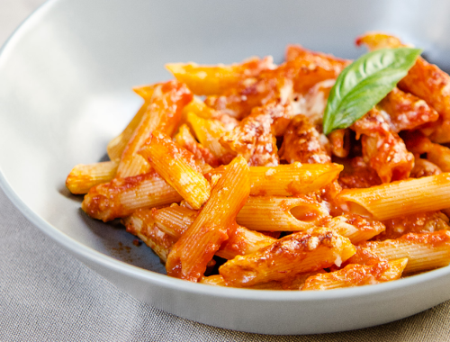 Mezze penne al sugo Sciuè Sciuè con pomodorini e basilico fresco in un piatto chiaro