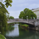 Visitare Lubiana in camper lungo il fiume Ljubljanica, battello che passa sotto un ponte nel centro storico
