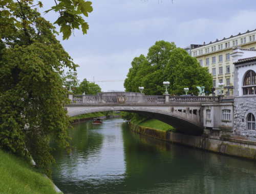 Visitare Lubiana in camper lungo il fiume Ljubljanica, battello che passa sotto un ponte nel centro storico