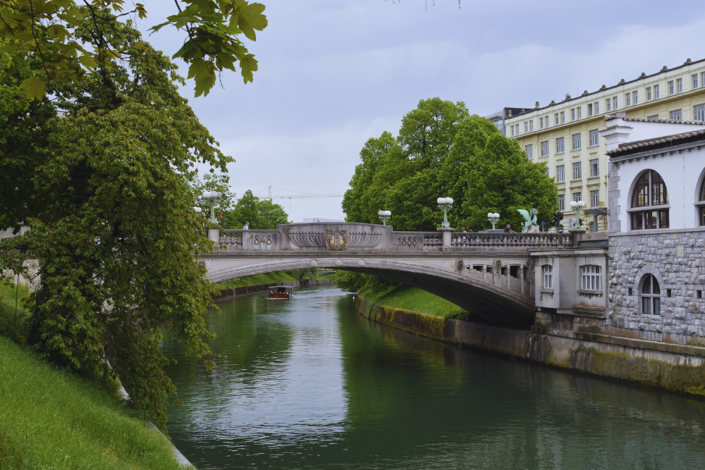 Visitare Lubiana in camper lungo il fiume Ljubljanica, battello che passa sotto un ponte nel centro storico