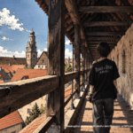 Illustrazione in stile manga di una ragazza di spalle con la maglietta di Attack on Titan sul camminamento delle mura di Nördlingen
